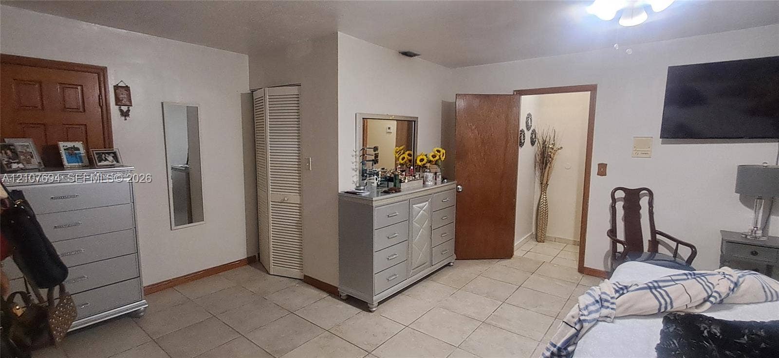 Interior space featuring neutral-toned tile flooring, solid wood doors, a white louvered closet door, and a ceiling-mounted light fixture
