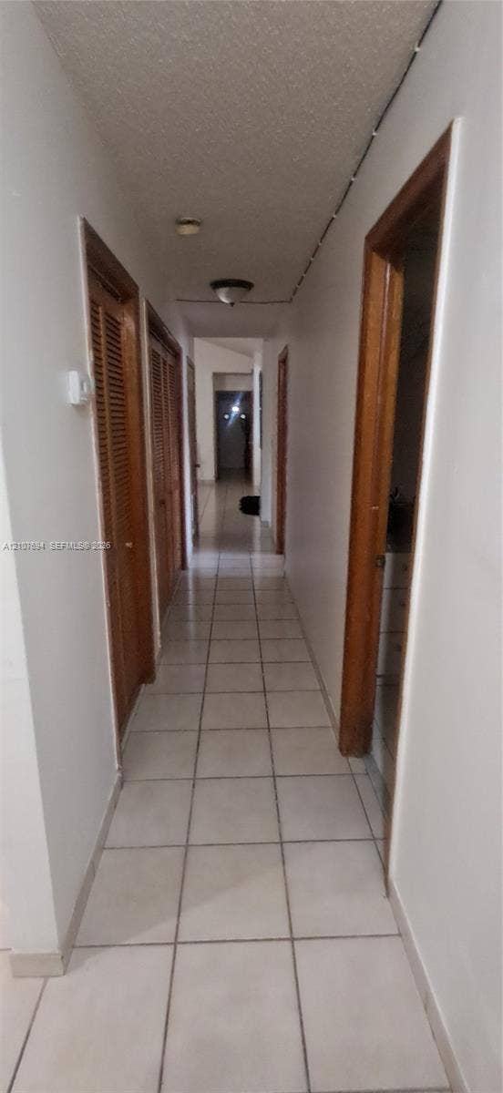Hallway featuring neutral-toned tile flooring, louvered wood-finish closet doors, and flush-mount lighting fixtures