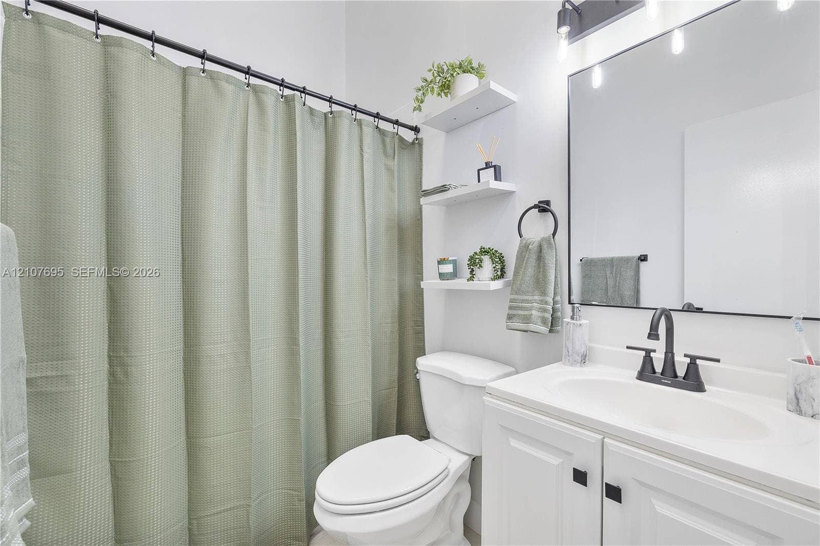 7198 Sportsmans Drive, North Lauderdale, FL 33068 Bathroom featuring a white vanity with a rectangular sink, matte black faucet, wall-mounted light fixture with glass shades, frameless mirror, and built-in shelving