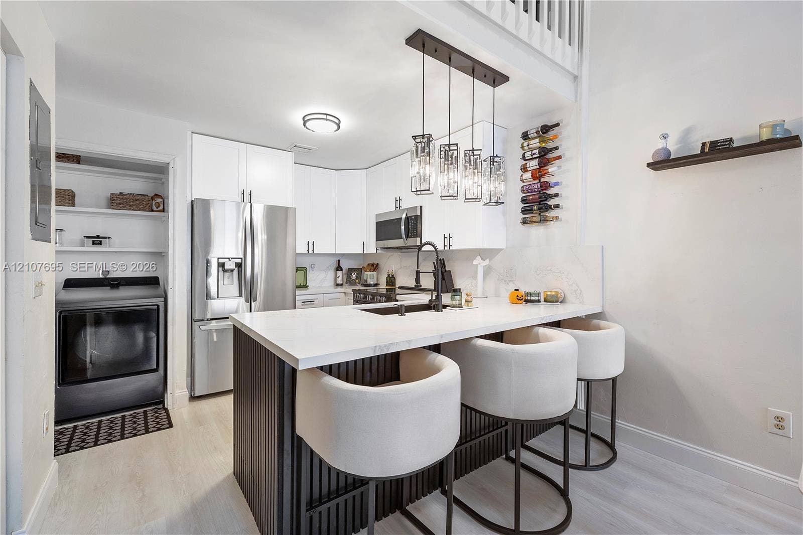 7198 Sportsmans Drive, North Lauderdale, FL 33068 Kitchen featuring white cabinetry, an island with a waterfall-edge countertop, matte black fixtures, stainless steel appliances, and a built-in wine rack
