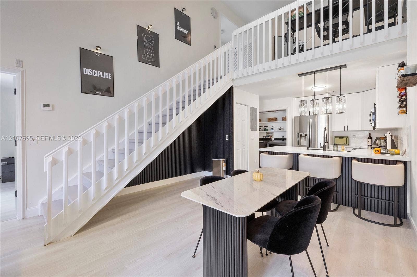 7198 Sportsmans Drive, North Lauderdale, FL 33068 Double-height ceiling with an open overlook, staircase featuring vertical slat paneling, white shaker-style cabinetry, breakfast bar with pendant lighting, and light-toned wood-finish flooring