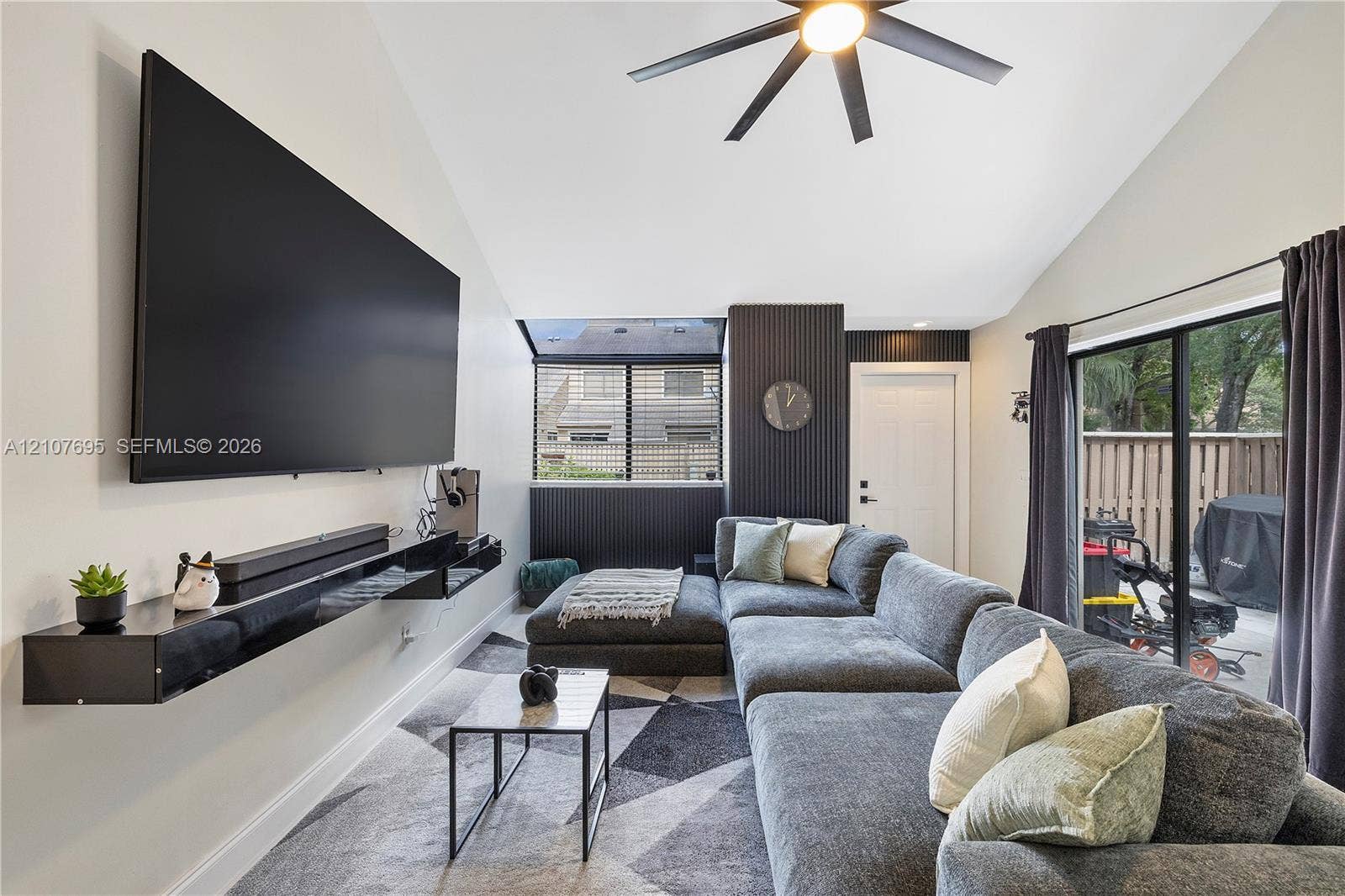 7198 Sportsmans Drive, North Lauderdale, FL 33068 Vaulted ceilings, dark accent wall with vertical slat detailing, matte black ceiling fan with integrated lighting, floating black media console, and sliding glass doors