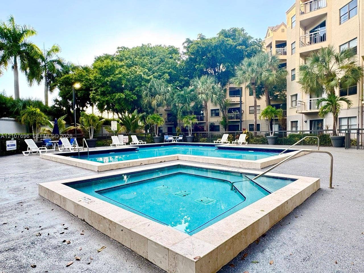 8290 Lake Drive, #418, Doral, FL 33166 In-ground swimming pool and spa featuring stone tile coping, surrounded by a paved deck and mature palm landscaping