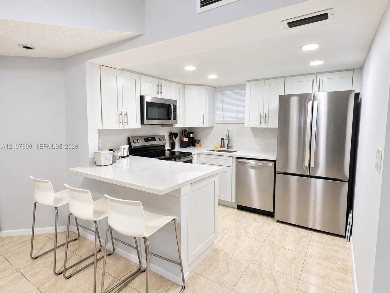 8290 Lake Drive, #418, Doral, FL 33166 Kitchen featuring white shaker-style cabinetry, quartz countertops, stainless steel appliances, recessed lighting, and tile flooring
