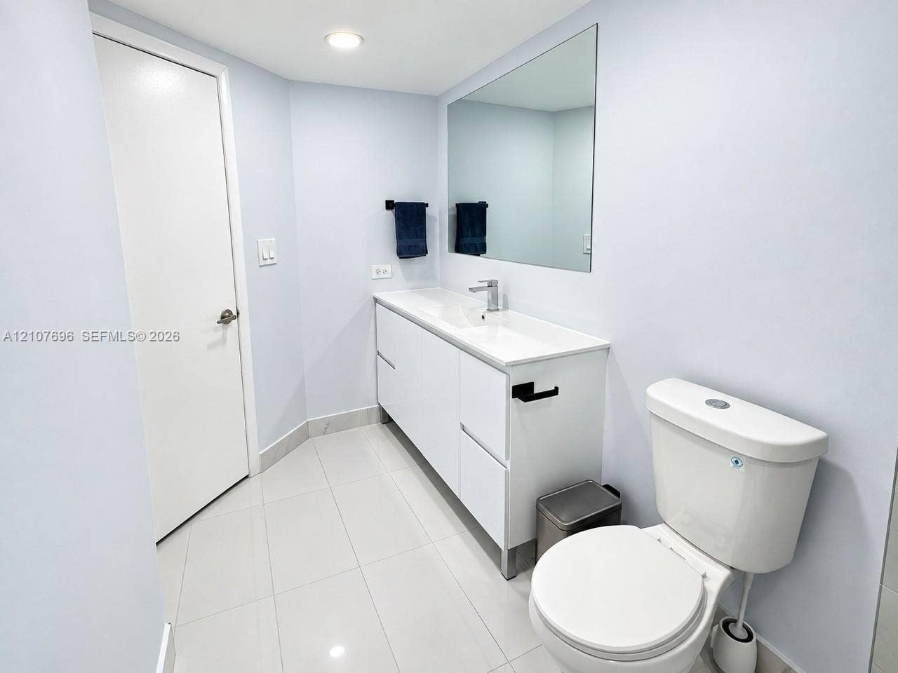 8290 Lake Drive, #418, Doral, FL 33166 Bathroom featuring white cabinetry, integrated sink, polished tile flooring, large wall-mounted mirror, and matte black fixtures
