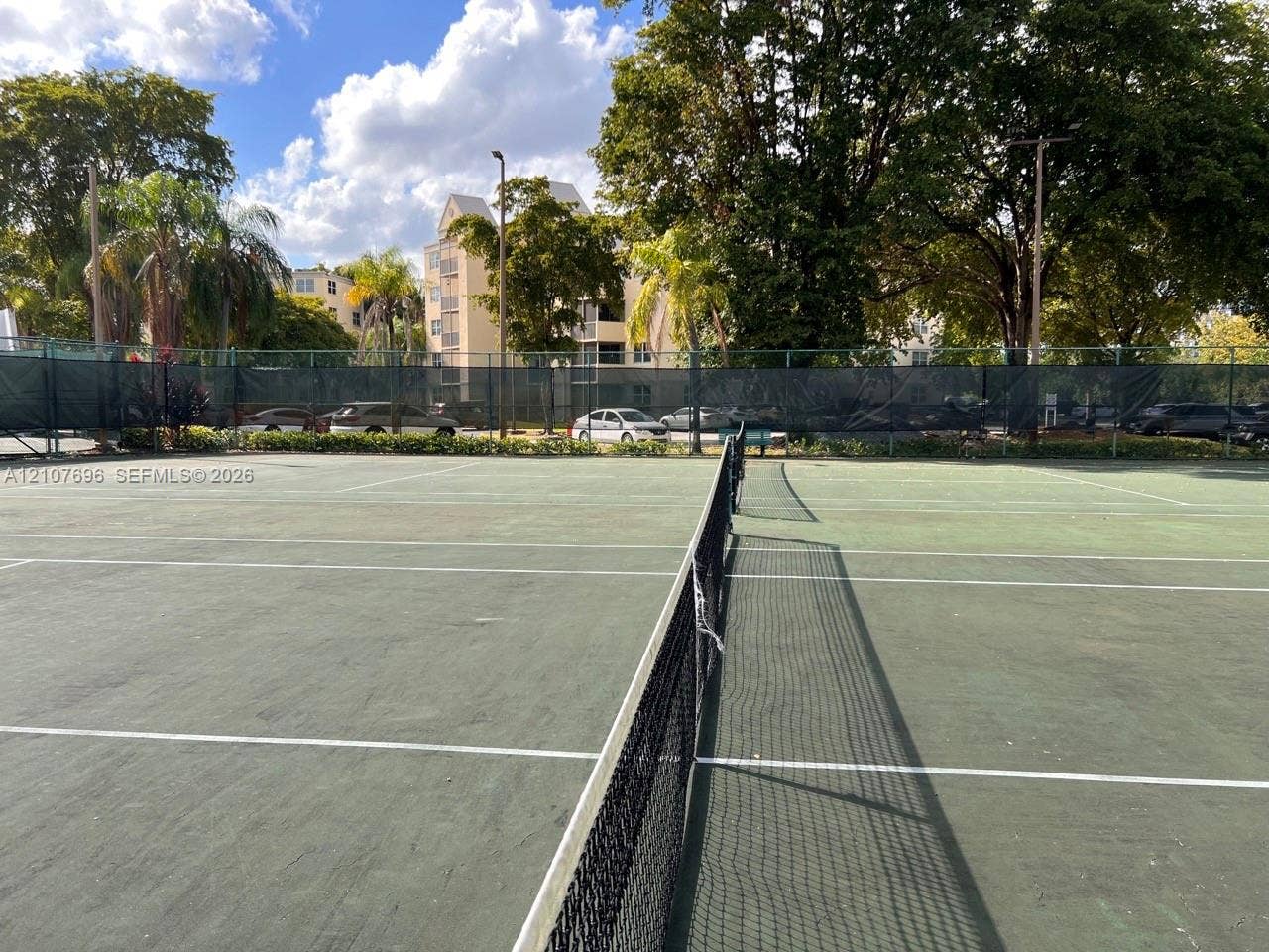 8290 Lake Drive, #418, Doral, FL 33166 Hard-court tennis facility featuring a central net, perimeter fencing, and mature trees
