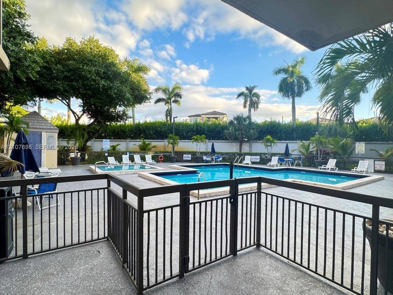 8290 Lake Drive, #418, Doral, FL 33166 Community pool and spa area featuring a paver deck, metal safety fencing, and established palm trees