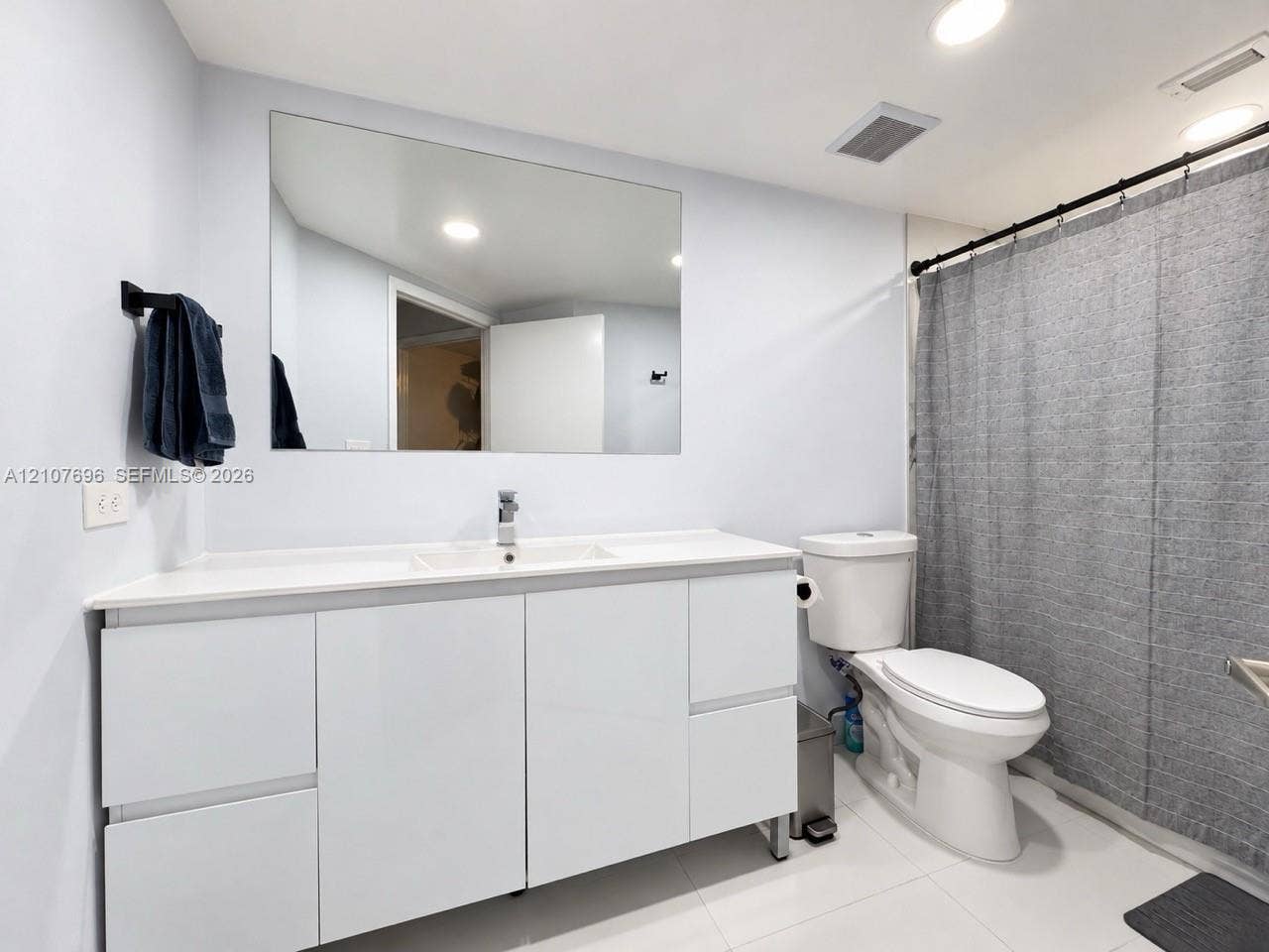 8290 Lake Drive, #418, Doral, FL 33166 Modern bathroom vanity with high-gloss white cabinetry, integrated sink, and polished chrome faucet featuring a large frameless wall mirror, recessed lighting, and tile flooring