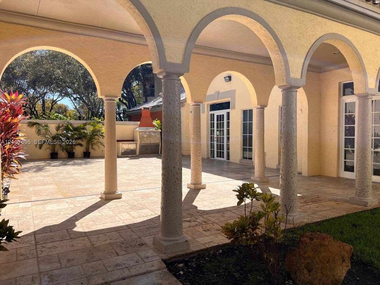 8290 Lake Drive, #418, Doral, FL 33166 Covered patio featuring structural stone columns, arched masonry detailing, paved flooring, and a built-in outdoor masonry grill