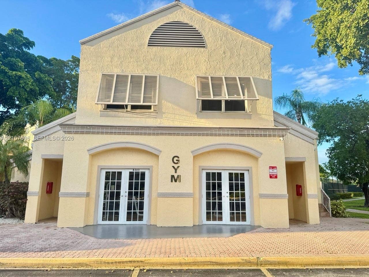 8290 Lake Drive, #418, Doral, FL 33166 Stucco exterior building featuring arched entryways, dual French doors with glass panes, decorative window shutters, and a semi-circular attic vent