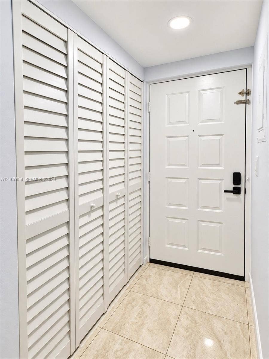 8290 Lake Drive, #418, Doral, FL 33166 Entryway featuring large-format tile flooring, a six-panel door with matte black hardware, and floor-to-ceiling storage cabinetry with louvered doors