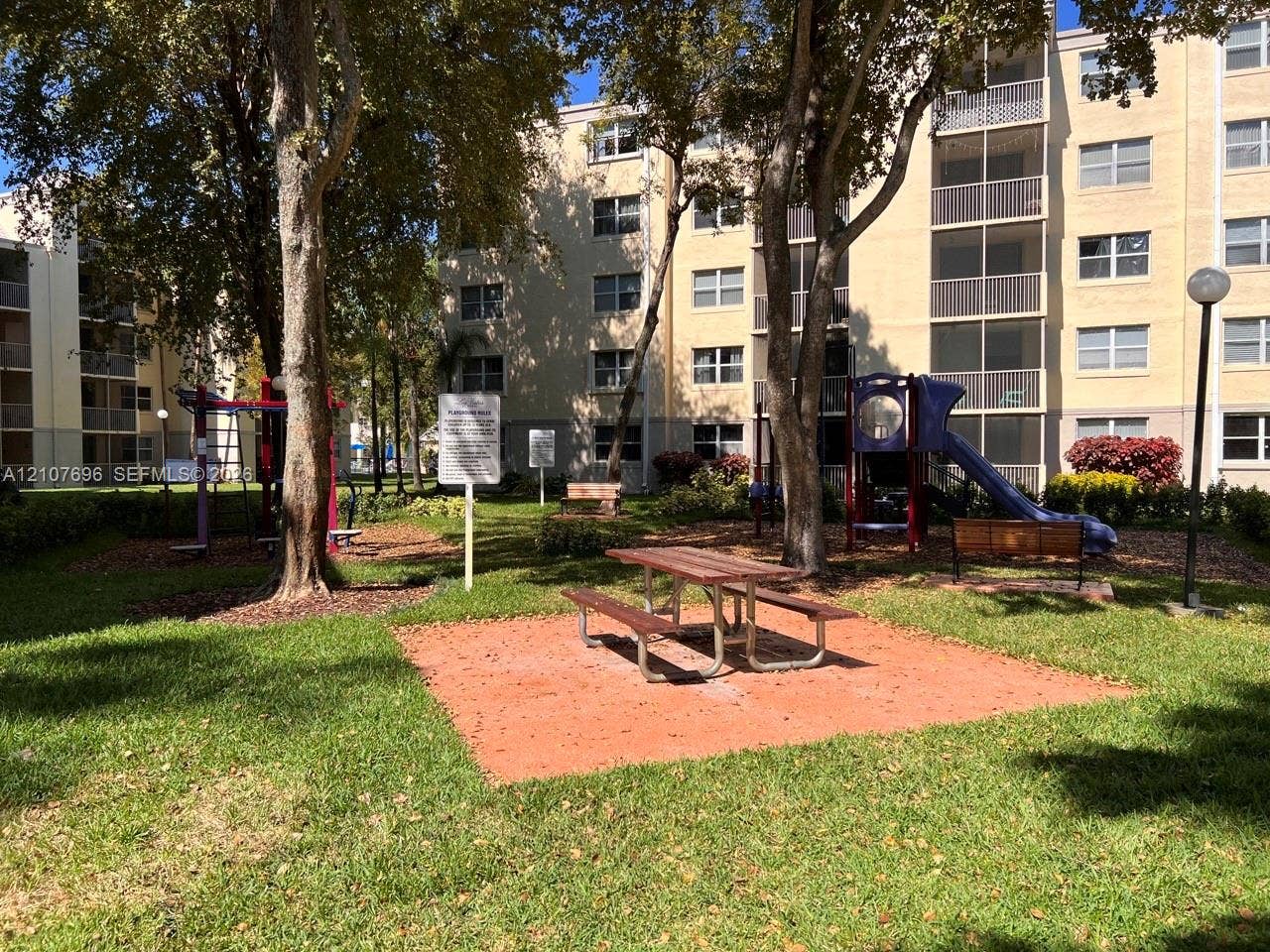 8290 Lake Drive, #418, Doral, FL 33166 Common area featuring a recreational playground, manicured lawn, mature trees, and a fixed metal picnic table