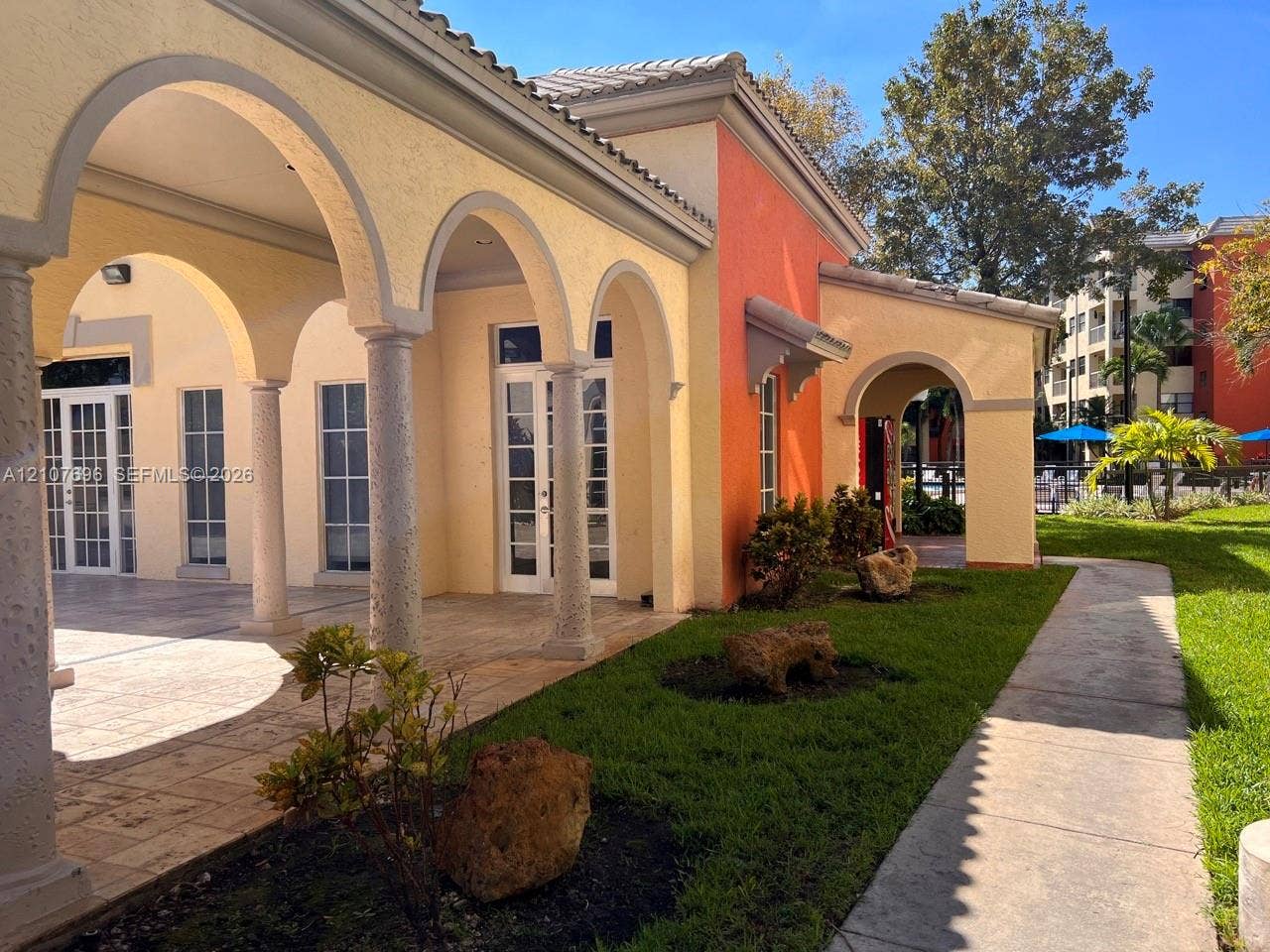 8290 Lake Drive, #418, Doral, FL 33166 Exterior facade featuring stucco walls, a covered colonnade with arched openings, stone-tile flooring, and glass-paneled double doors
