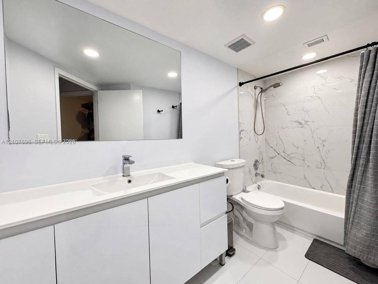 8290 Lake Drive, #418, Doral, FL 33166 Modern bathroom featuring a high-gloss white vanity with a rectangular sink, large format mirror, stone-finish tile shower surround, and recessed ceiling lighting