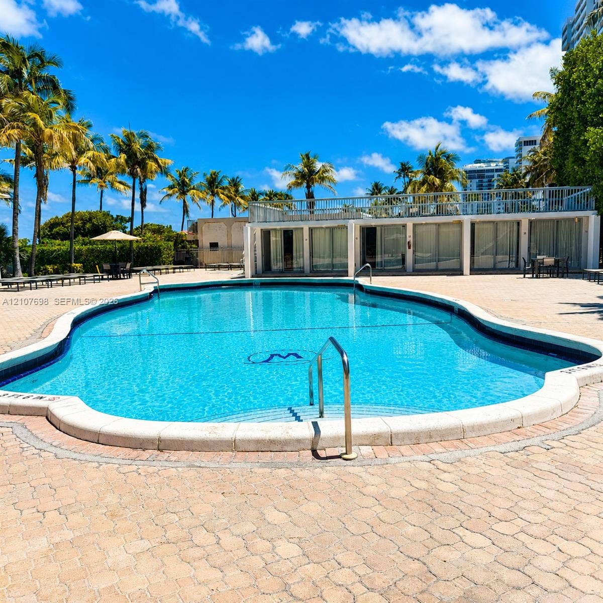 In-ground swimming pool with stone-tiled deck, metal handrails, and upper-level terrace with metal railing