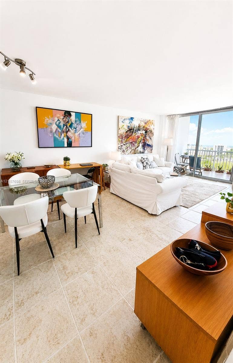 Open-concept room featuring light-toned tile flooring, adjustable multi-head track lighting, floor-to-ceiling glass sliding doors, and a private balcony with metal railing
