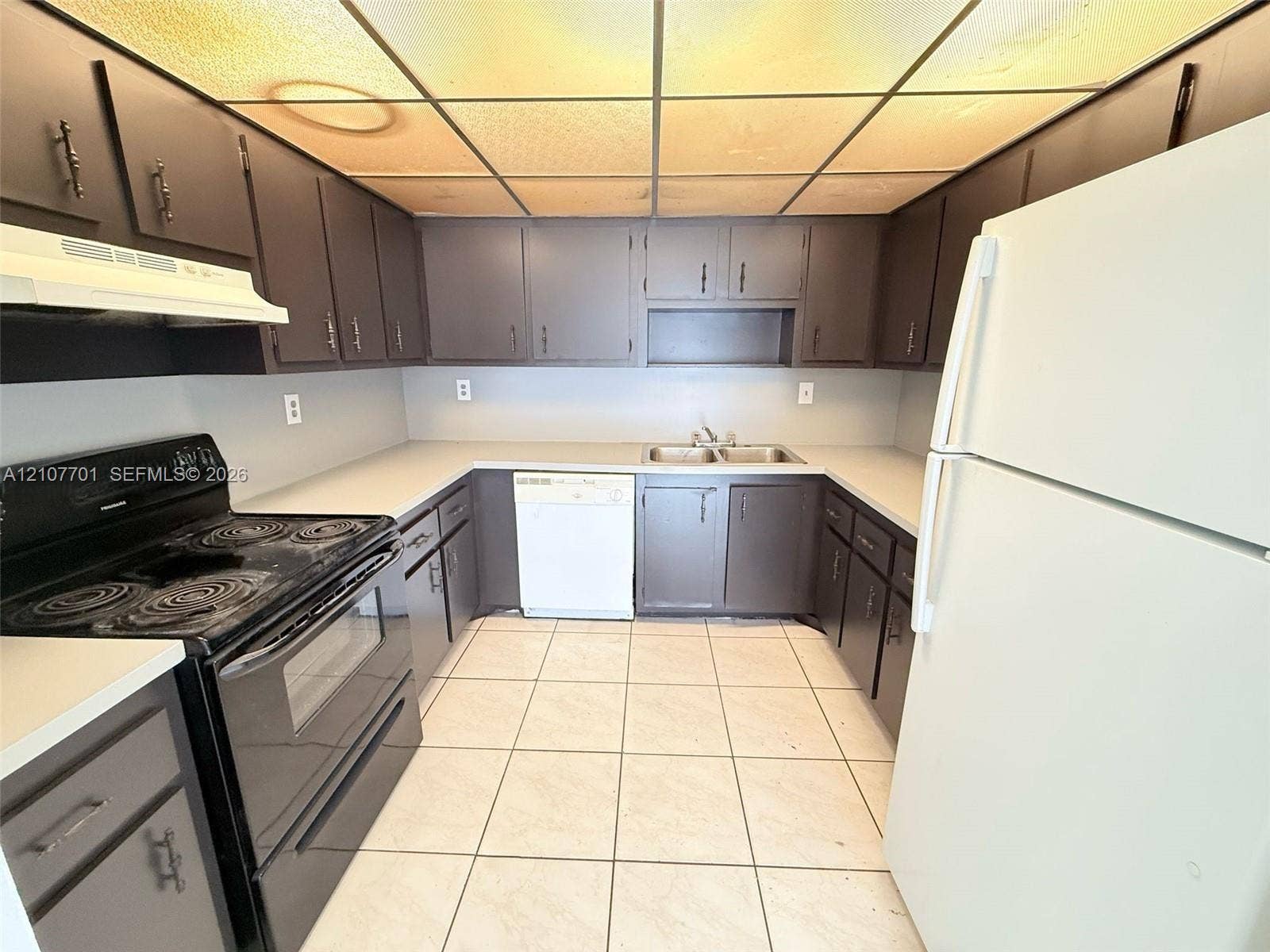3100 Coral Springs Drive, #2B, Coral Springs, FL 33065 Kitchen featuring dark cabinetry, expansive solid-surface countertops, tile flooring, and integrated dual-basin stainless steel sink