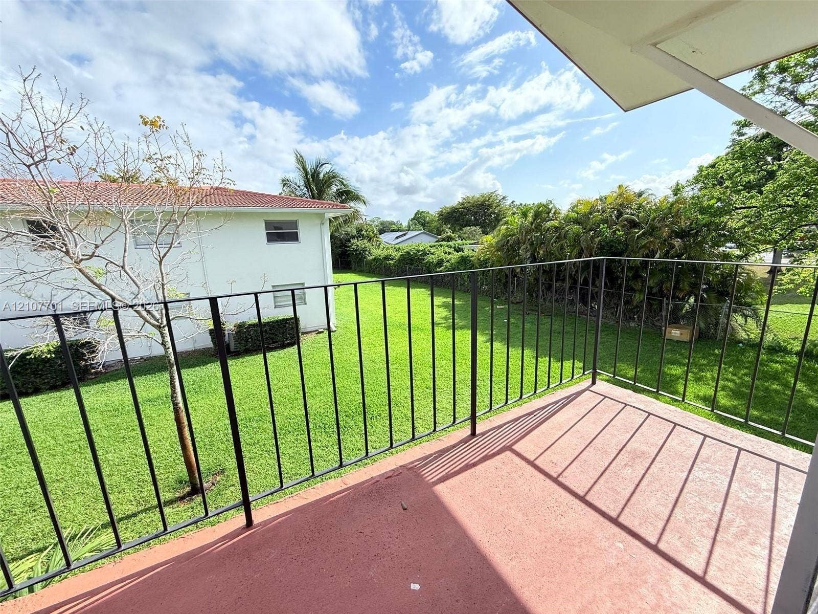 3100 Coral Springs Drive, #2B, Coral Springs, FL 33065 Covered exterior balcony featuring a solid concrete surface and black metal railing, overlooking a large grass lawn