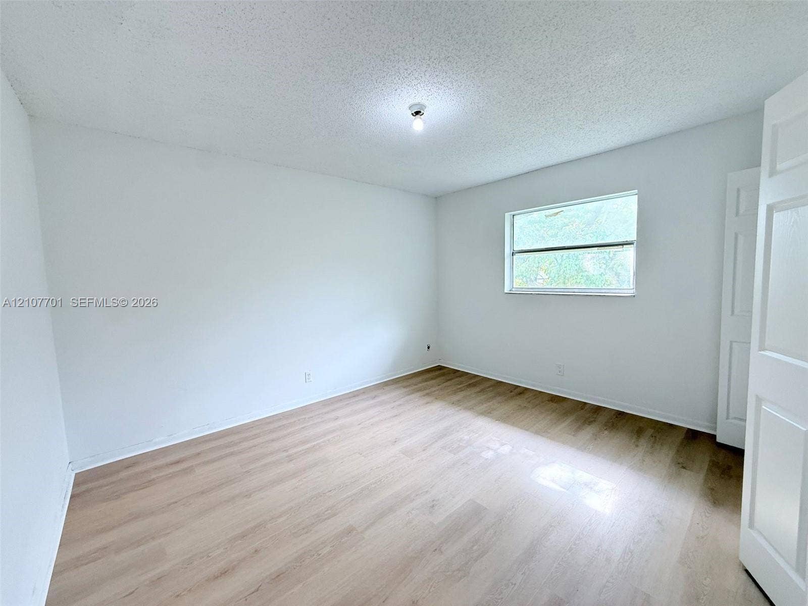3100 Coral Springs Drive, #2B, Coral Springs, FL 33065 Neutral-toned interior featuring wood-finish flooring, a single horizontal window, and a white multi-panel interior door