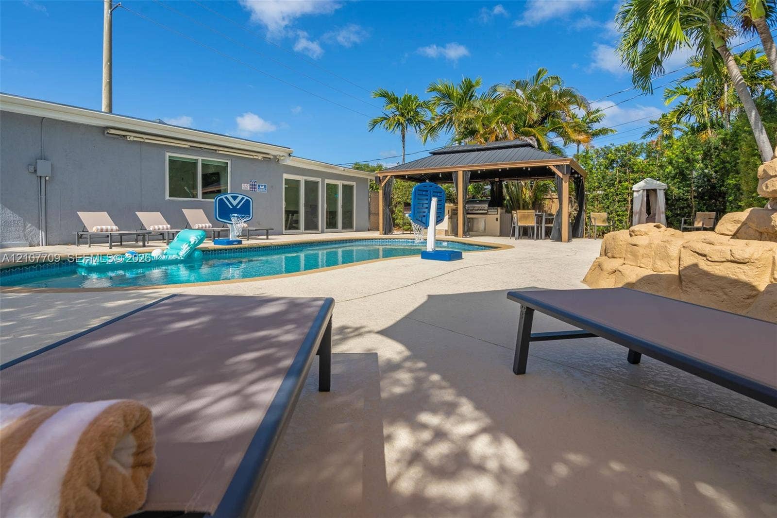 In-ground swimming pool with stone-textured accents, covered outdoor gazebo, and concrete patio surround
