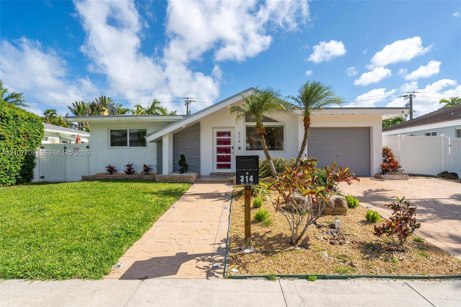 Single-story residence featuring a mid-century modern aesthetic, stamped concrete driveway and walkway, attached garage, and xeriscaped front garden with mature palm trees