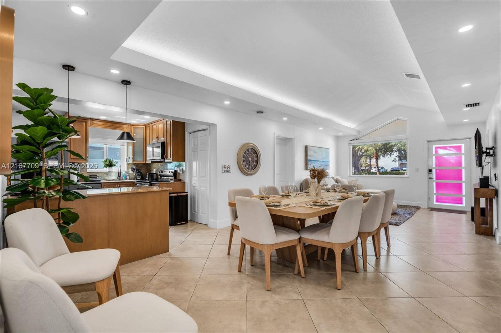 Open-concept interior featuring vaulted ceilings with recessed lighting, tile flooring, wood-finish cabinetry, and a glass-paneled entry door