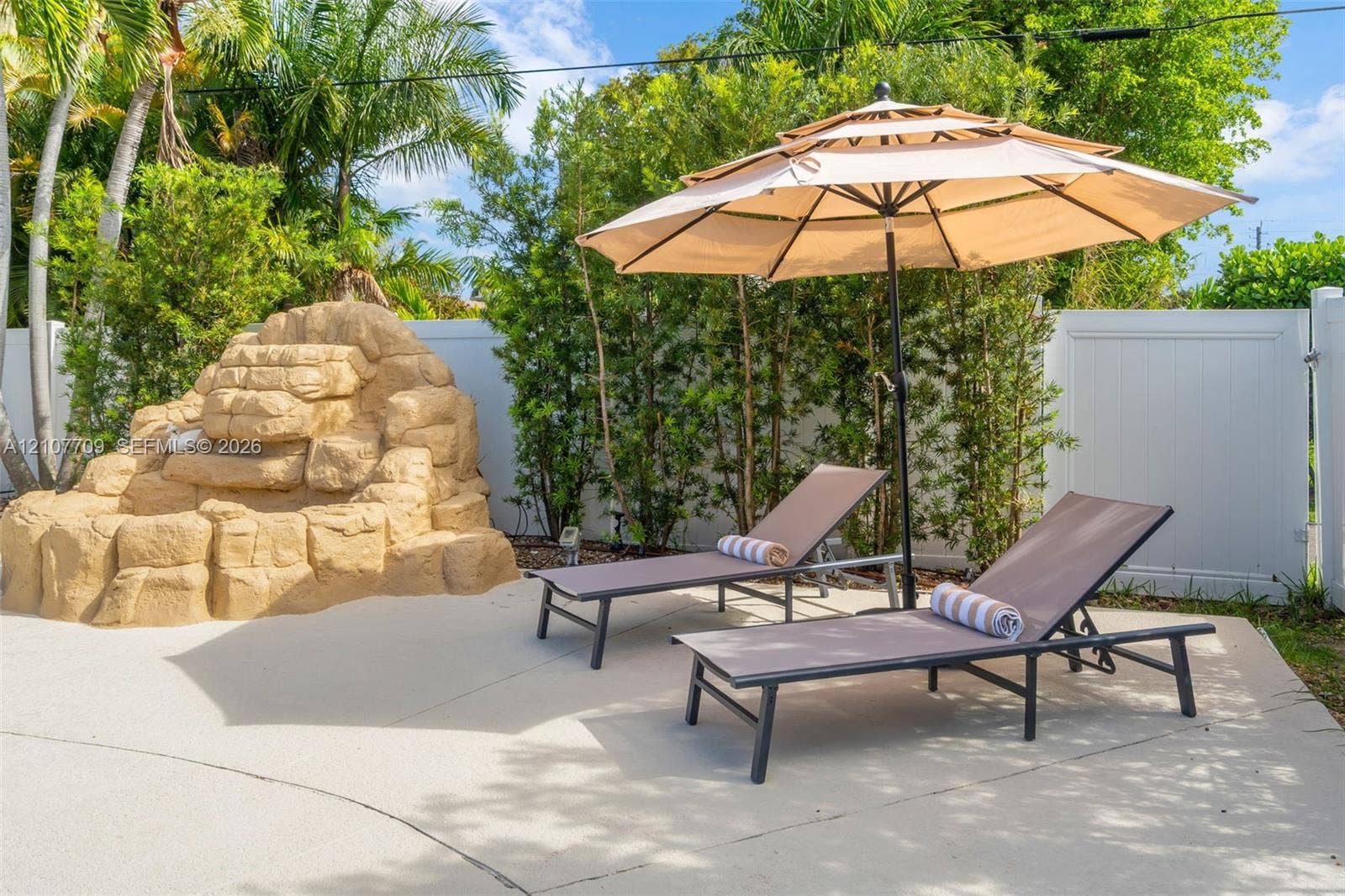 Outdoor patio featuring a custom stone waterfall feature, privacy fencing, and mature landscaping