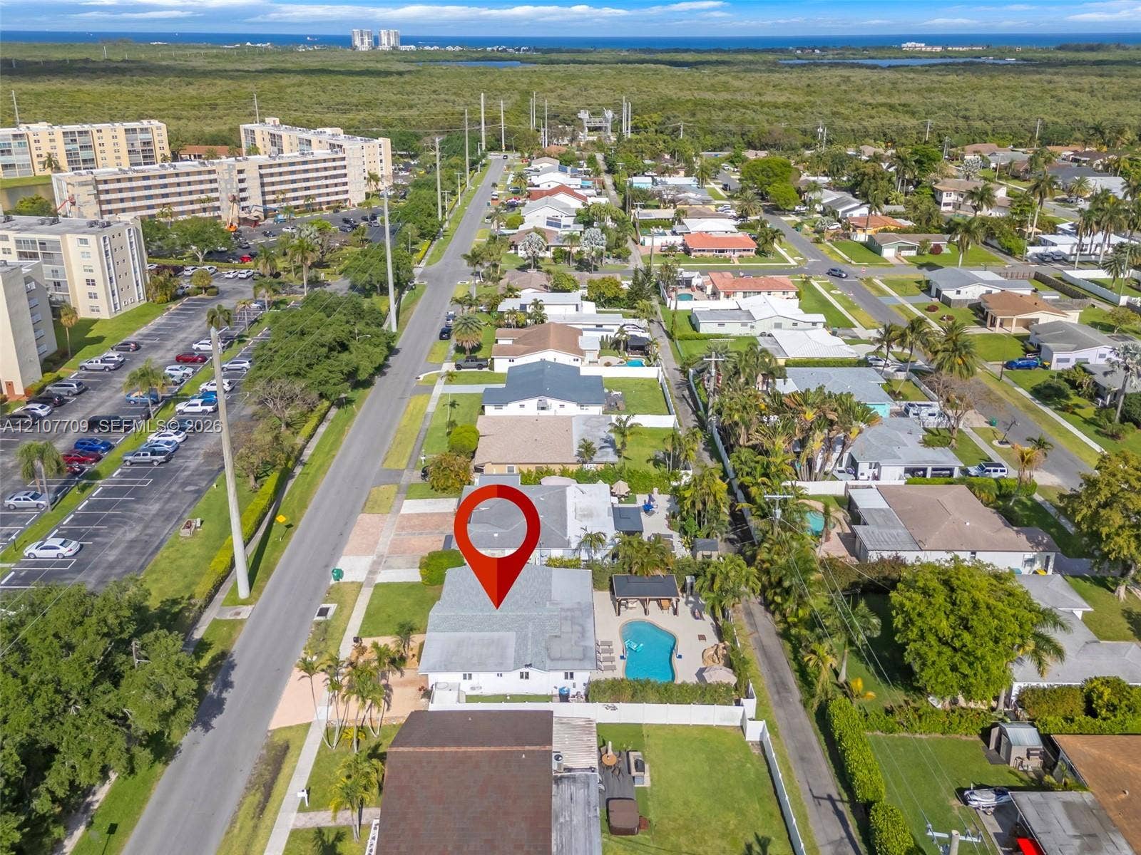 Aerial perspective showcasing a coastal property featuring an in-ground swimming pool, paved patio, mature landscaping, and an expansive lawn