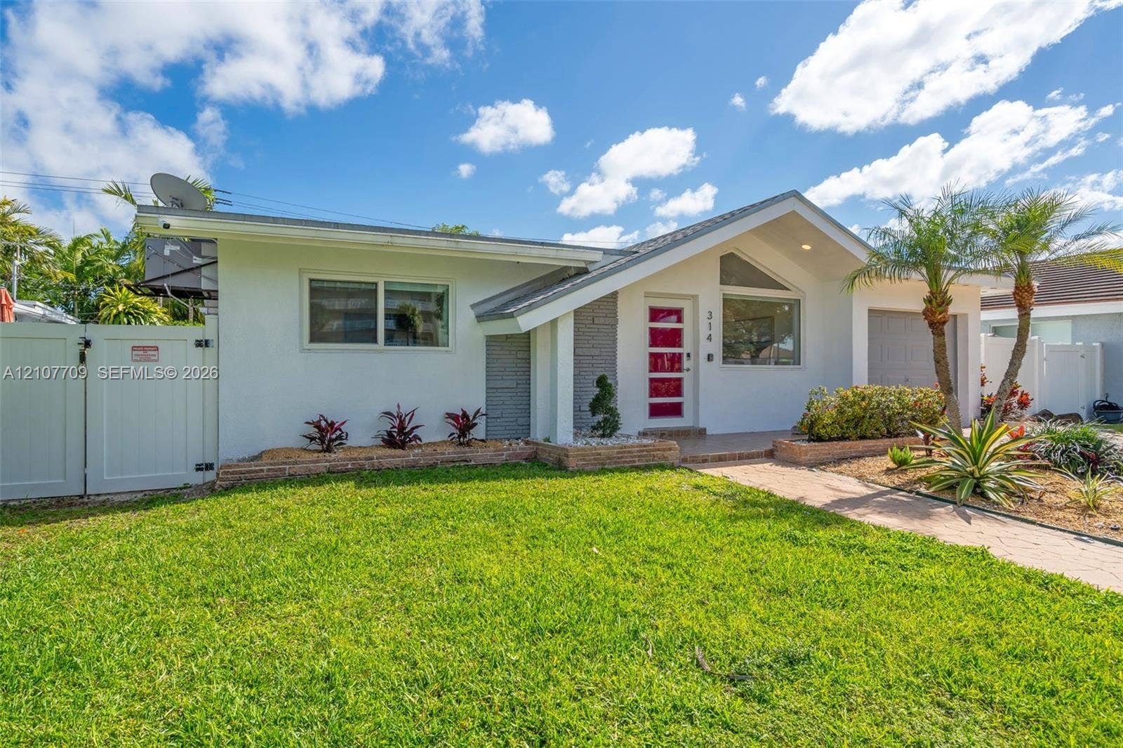Single-story residence featuring a mid-century inspired roofline, white exterior finish with textured stone accents, a multi-pane red entry door, and a paved walkway leading to the home