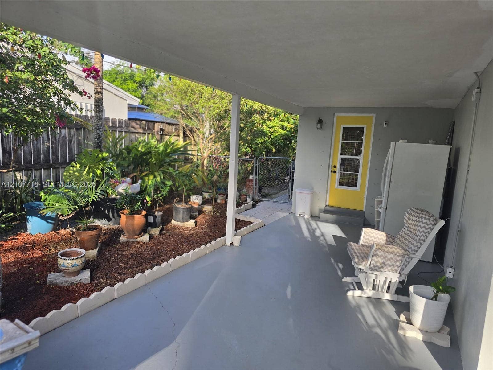 2321 N 57th Avenue, Hollywood, FL 33021 Covered concrete patio featuring a scalloped concrete landscape border, wood-mulch garden bed, and a exterior door with a multi-pane glass insert