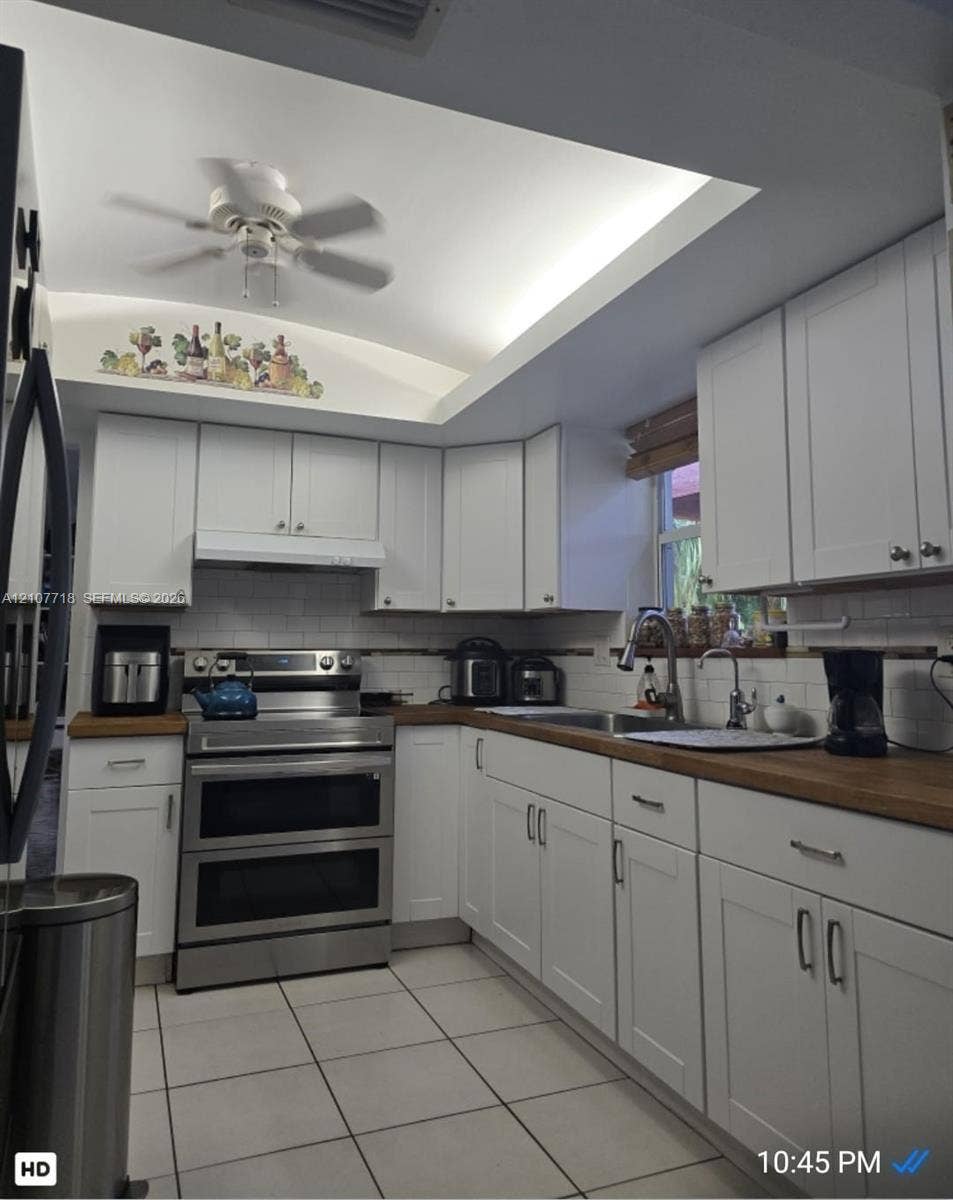 2321 N 57th Avenue, Hollywood, FL 33021 White cabinetry with shaker-style doors, wood-finish countertops, stainless steel dual-oven range, subway tile backsplash, and recessed tray ceiling with integrated lighting