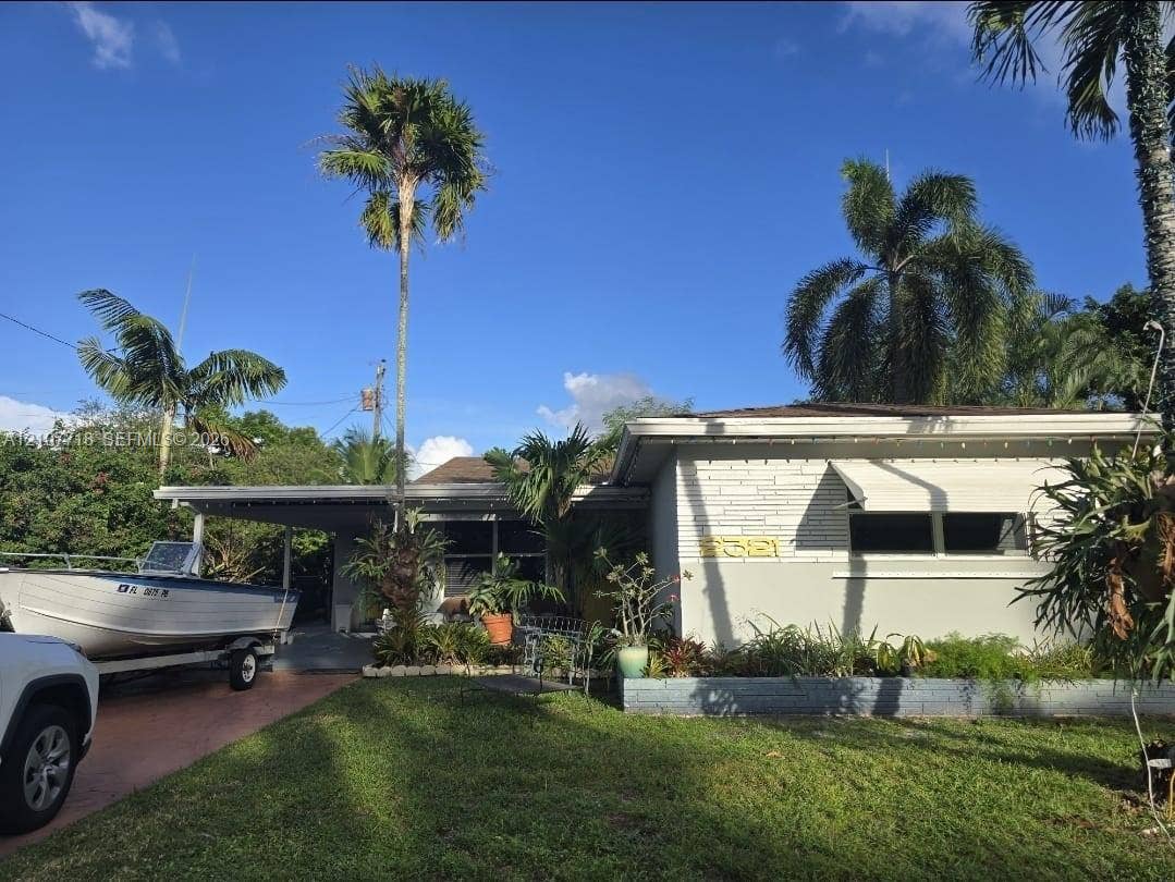 2321 N 57th Avenue, Hollywood, FL 33021 Single-story residence featuring a painted masonry facade, metal awning window coverings, a covered carport, and established tropical landscaping