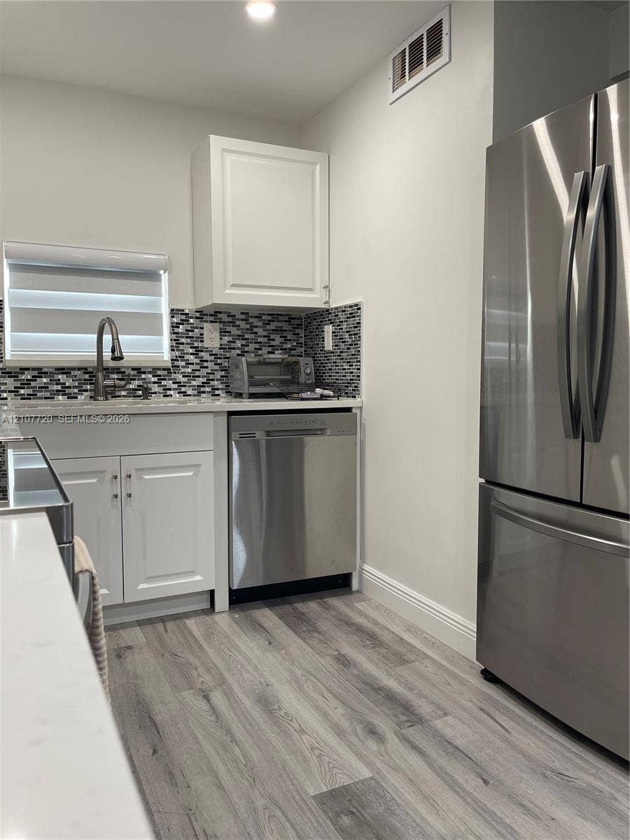 8921 S Hollybrook Boulevard, #204, Pembroke Pines, FL 33025 Kitchen featuring white shaker-style cabinetry, wood-finish flooring, stainless steel appliances, and a mosaic tile backsplash
