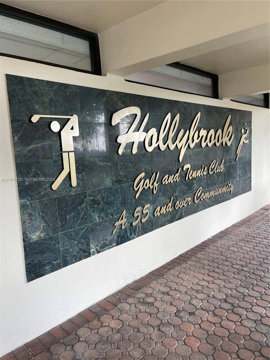 8921 S Hollybrook Boulevard, #204, Pembroke Pines, FL 33025 Stone-tiled signage featuring metallic lettering and integrated golf and tennis iconography, set against a paved brick walkway