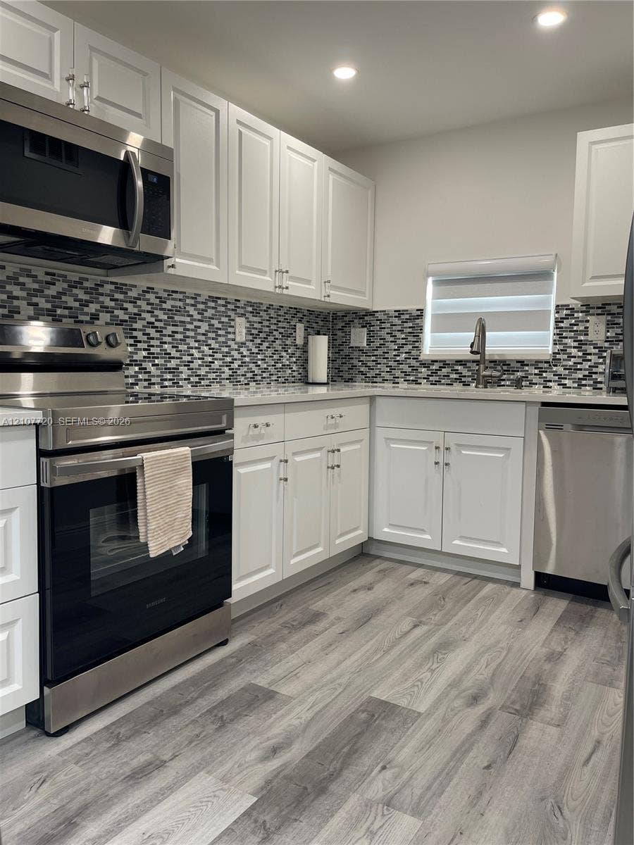 8921 S Hollybrook Boulevard, #204, Pembroke Pines, FL 33025 Kitchen featuring white shaker-style cabinetry, stainless steel appliances, multi-tonal mosaic tile backsplash, stone-finish countertops, and wood-finish flooring
