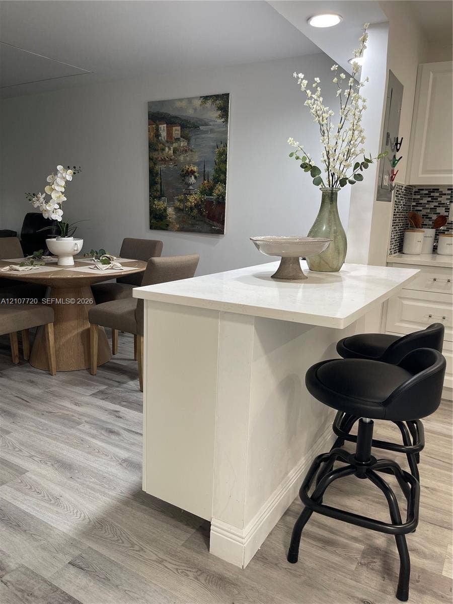 8921 S Hollybrook Boulevard, #204, Pembroke Pines, FL 33025 Kitchen peninsula featuring a white countertop and white cabinetry, complemented by wood-finish flooring and a multi-toned mosaic tile backsplash