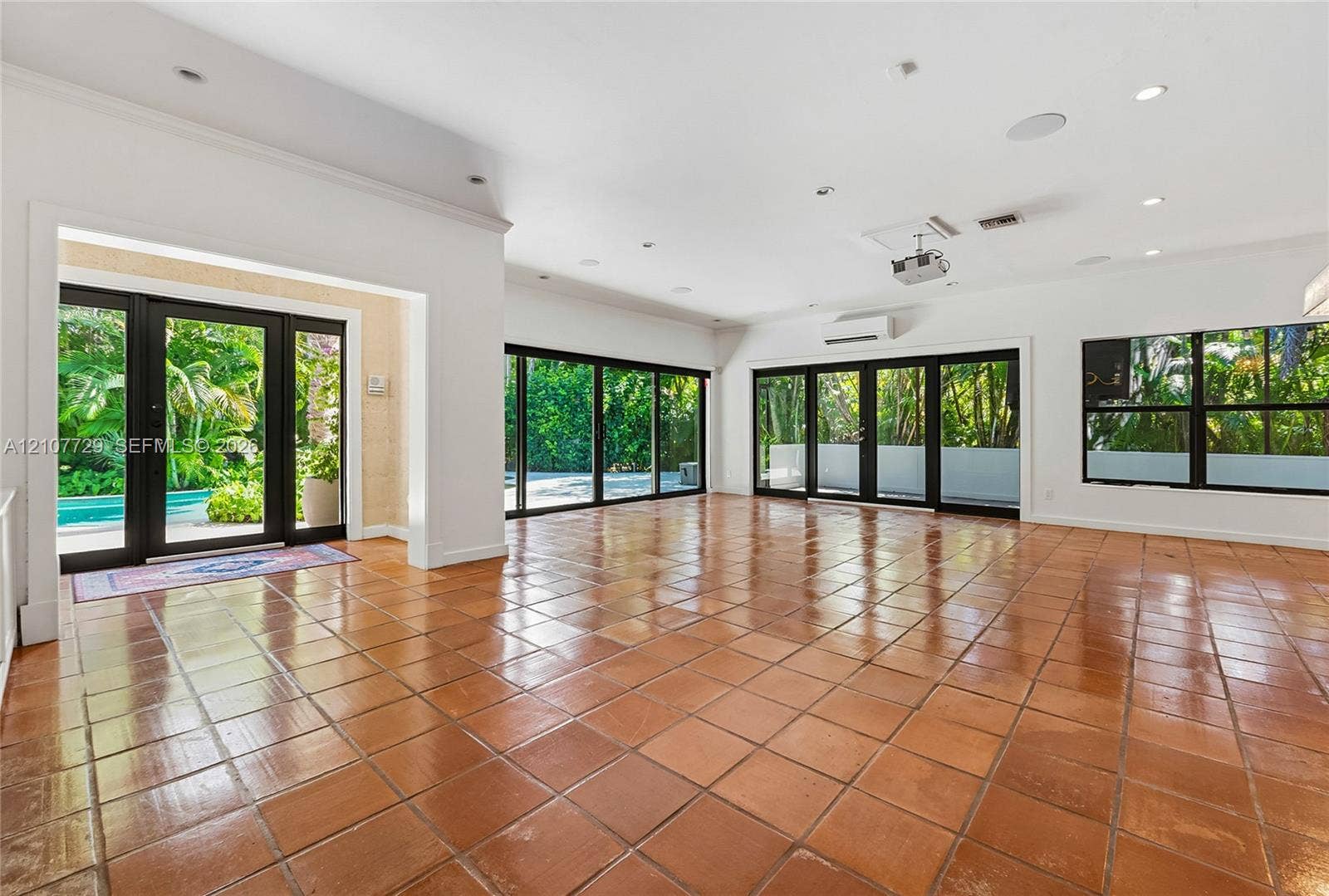 Open-concept interior featuring large-format ceramic tile flooring, multi-panel sliding glass doors, recessed lighting, and a wall-mounted climate control unit