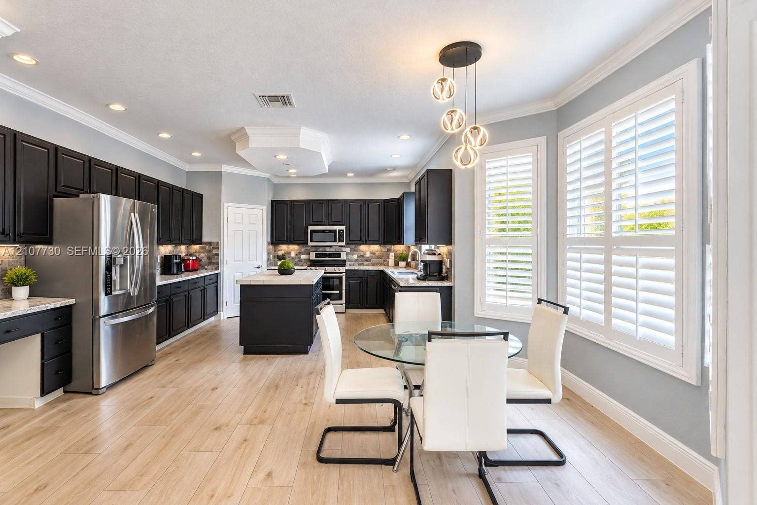 15606 SW 52nd Court, Miramar, FL 33027 Kitchen featuring dark cabinetry, stone-finish countertops, stainless steel appliances, wood-finish flooring, and crown molding