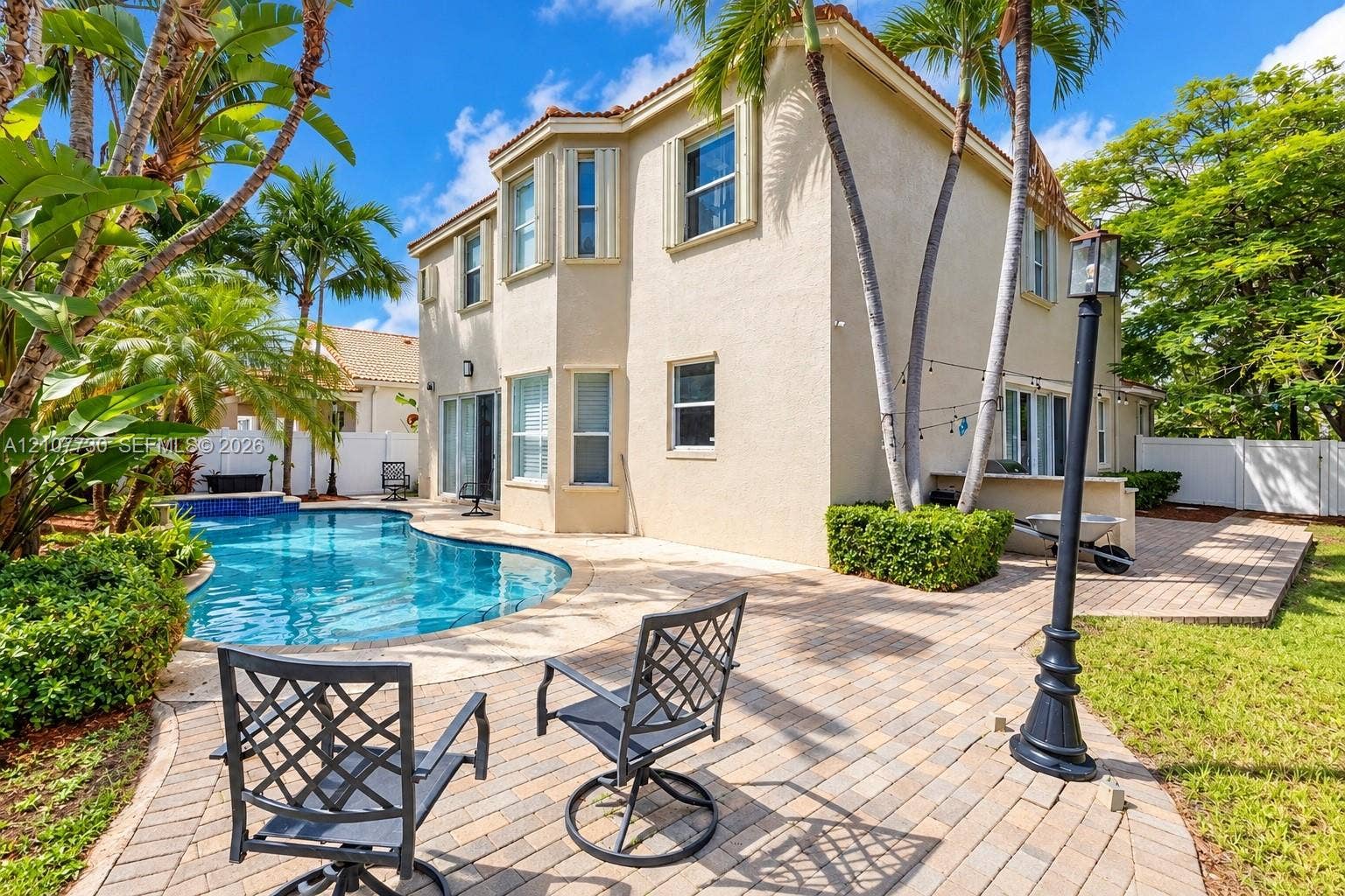 15606 SW 52nd Court, Miramar, FL 33027 Stucco exterior featuring a two-story bay window, paved patio, in-ground swimming pool, and mature palm trees