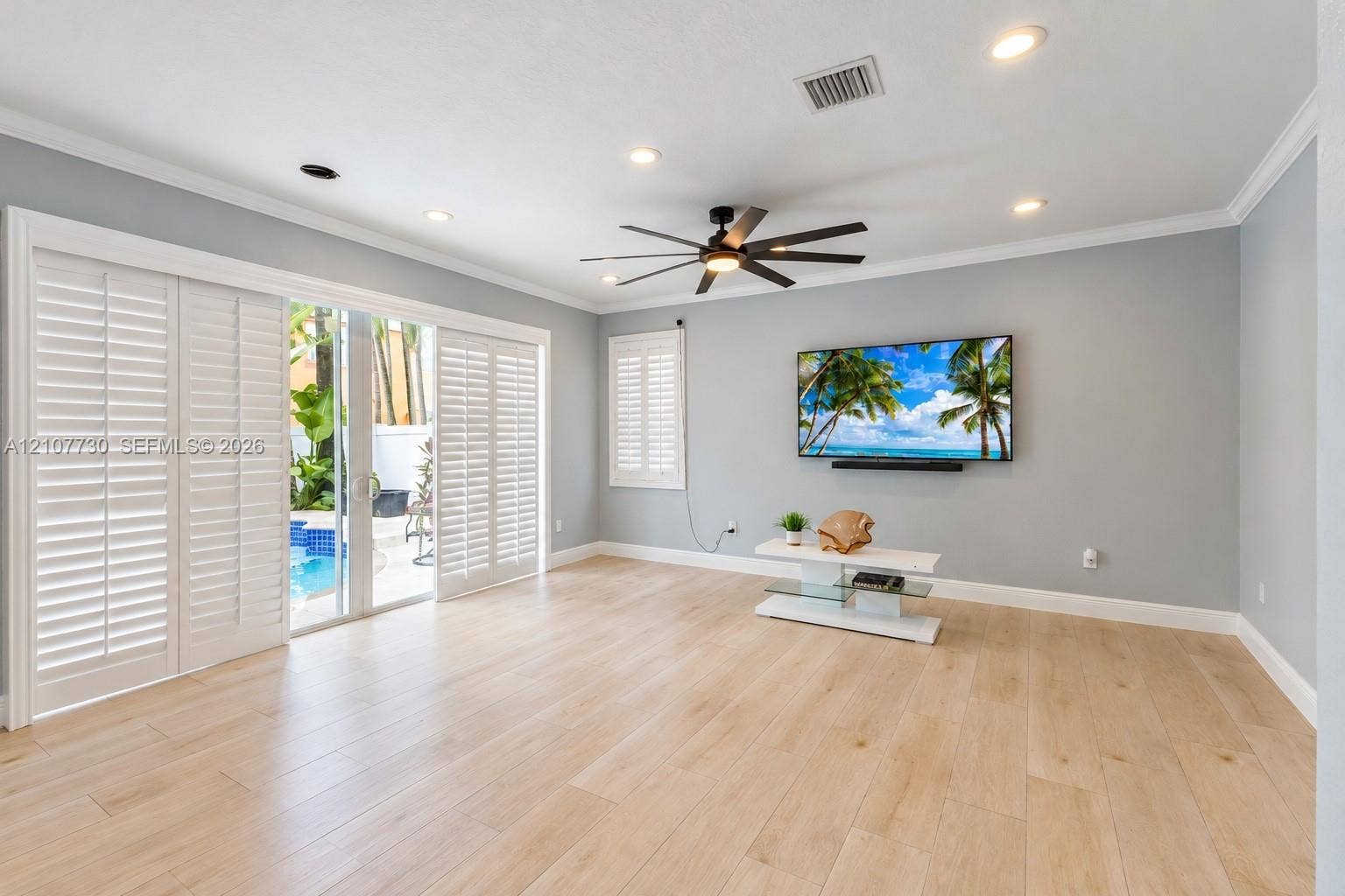 15606 SW 52nd Court, Miramar, FL 33027 Open-concept room featuring light wood-finish flooring, recessed lighting, a modern ceiling fan, sliding glass doors with plantation shutters, and crown molding