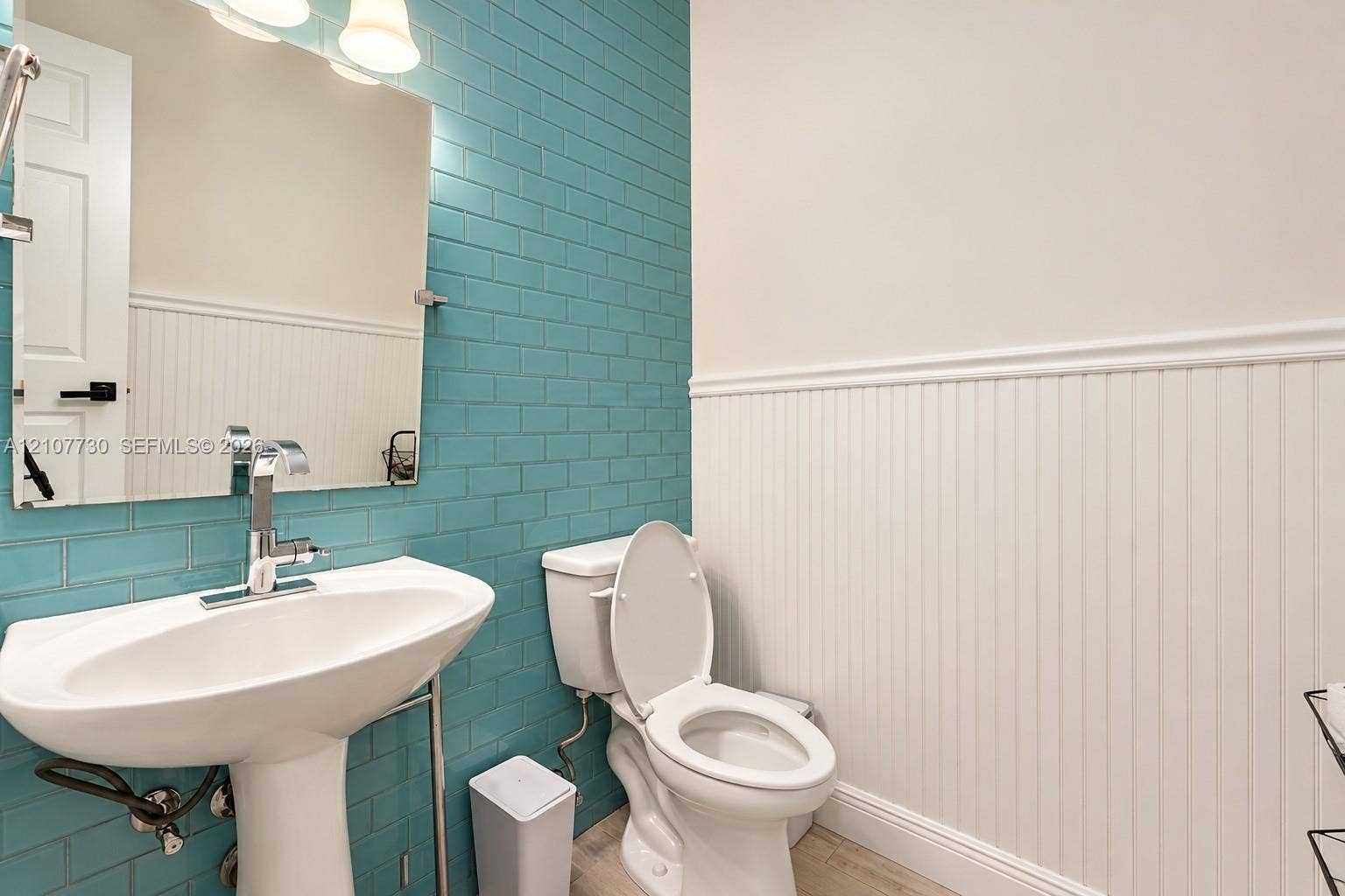 15606 SW 52nd Court, Miramar, FL 33027 Bathroom featuring a pedestal sink with a chrome finish faucet, blue subway tile backsplash, white beadboard wainscoting, and a wall-mounted mirror