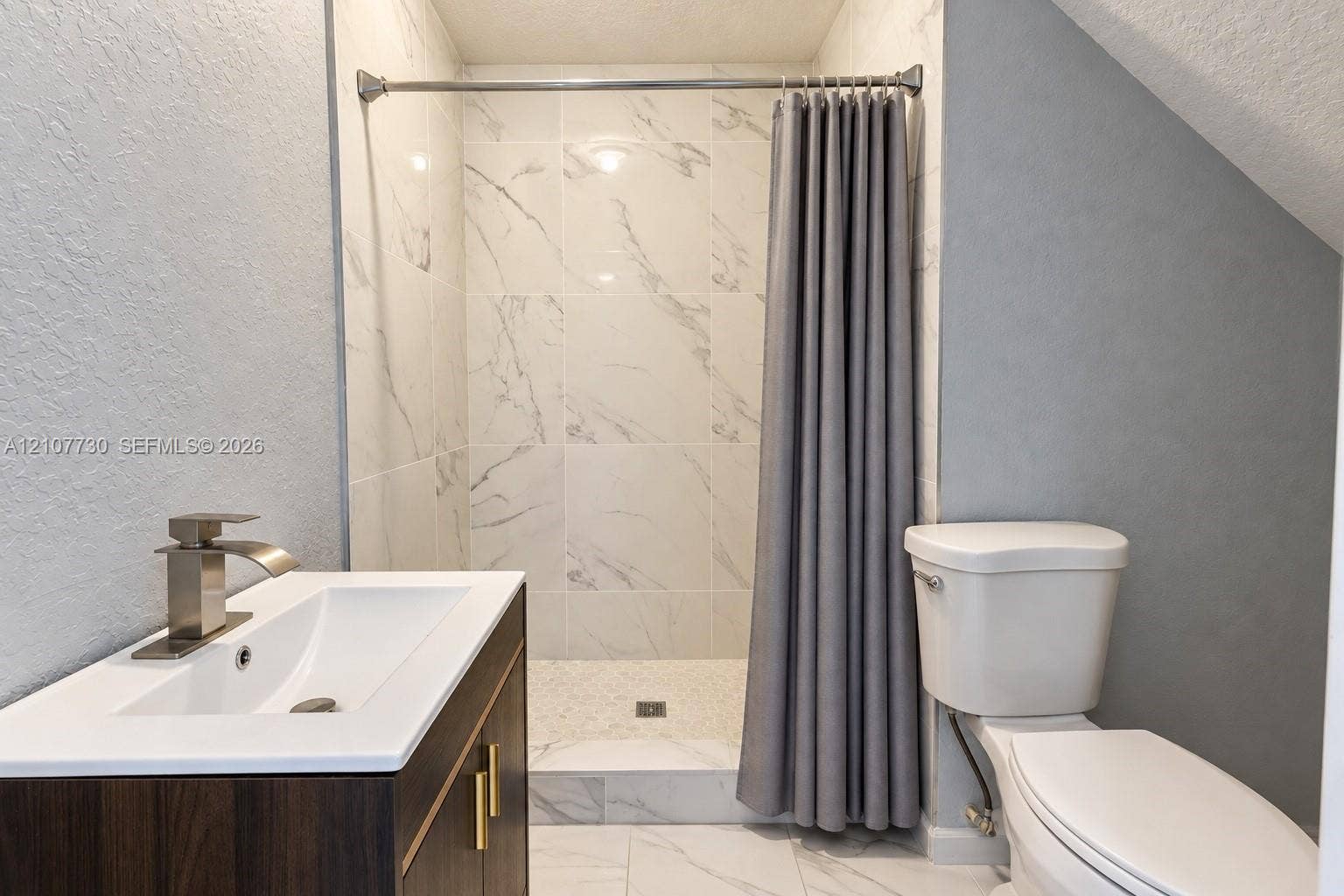 15606 SW 52nd Court, Miramar, FL 33027 Bathroom featuring a wood-finish vanity with a rectangular sink, matte metallic faucet, large-format tiled shower surround with stone-pattern detail, and stone-finish floor tiling