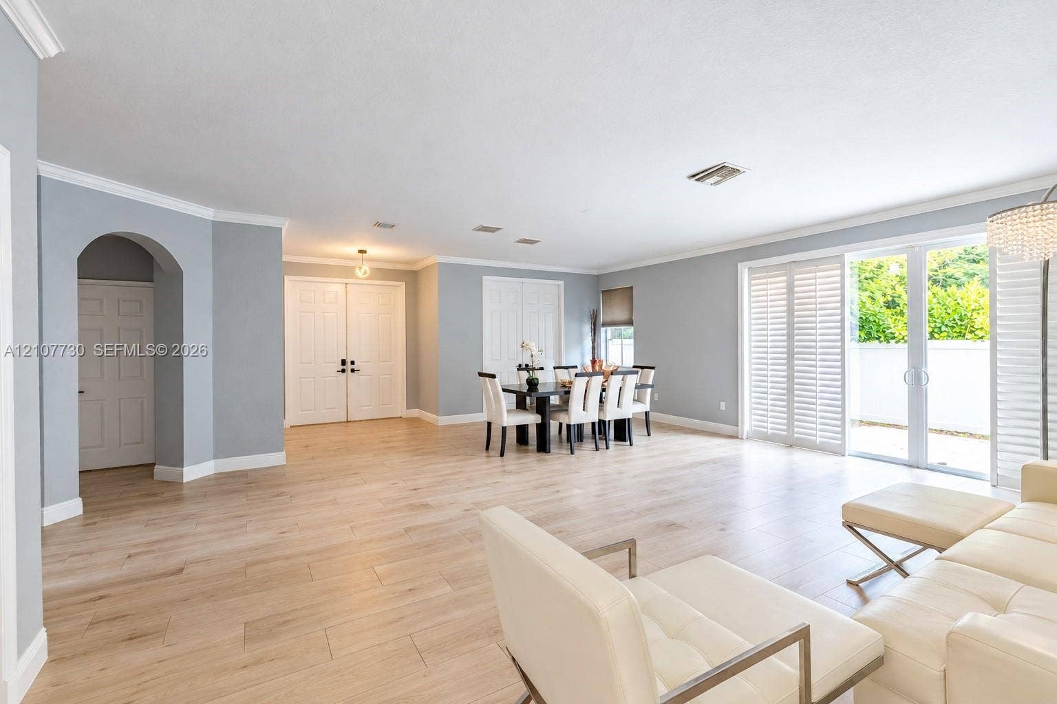 15606 SW 52nd Court, Miramar, FL 33027 Open-concept living space featuring wood-finish flooring, crown molding, arched entryway, and multi-panel sliding glass doors with plantation shutters