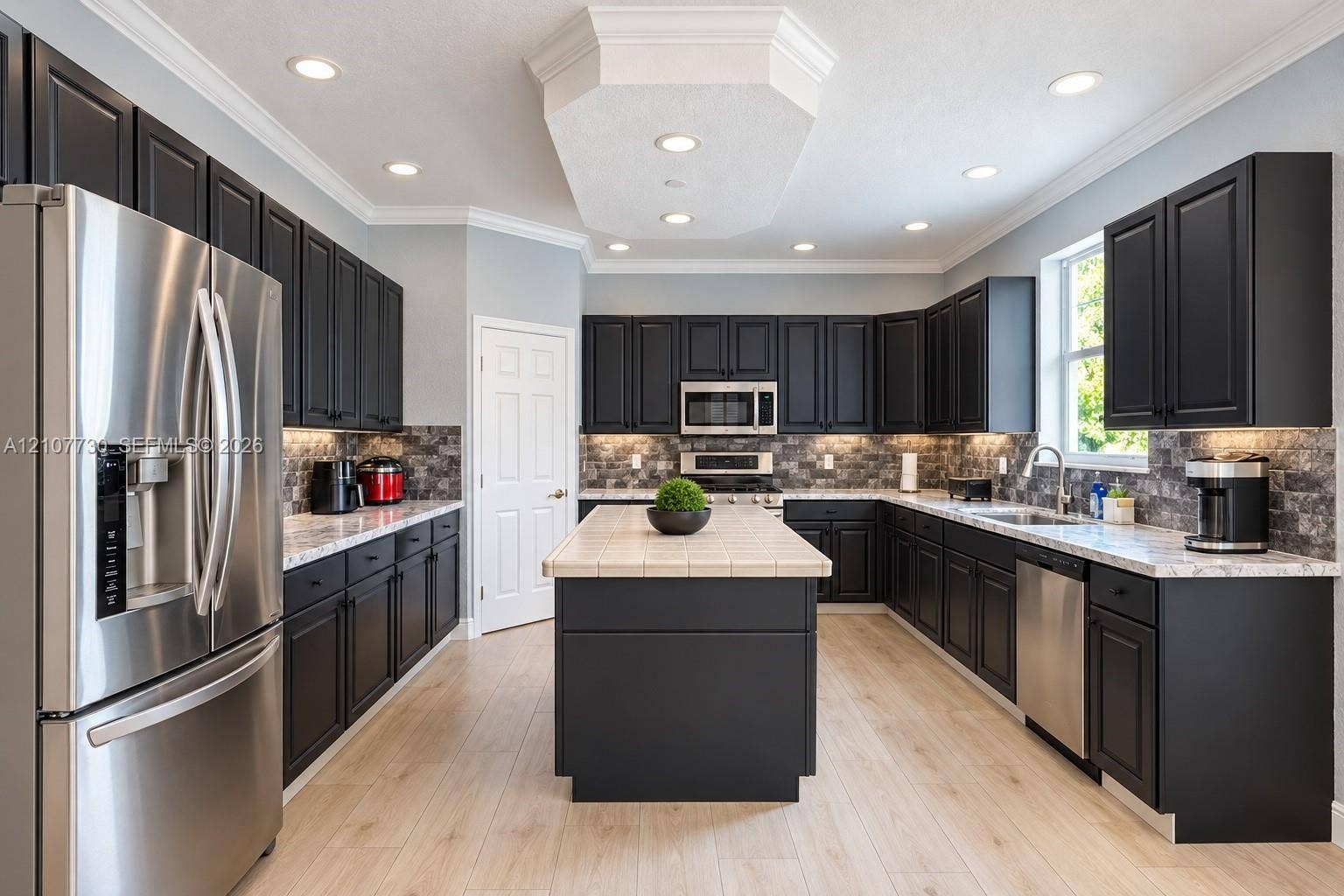 15606 SW 52nd Court, Miramar, FL 33027 Kitchen featuring dark-toned cabinetry, light-toned countertops, tile-topped center island, stone-finish backsplash, and stainless steel appliances