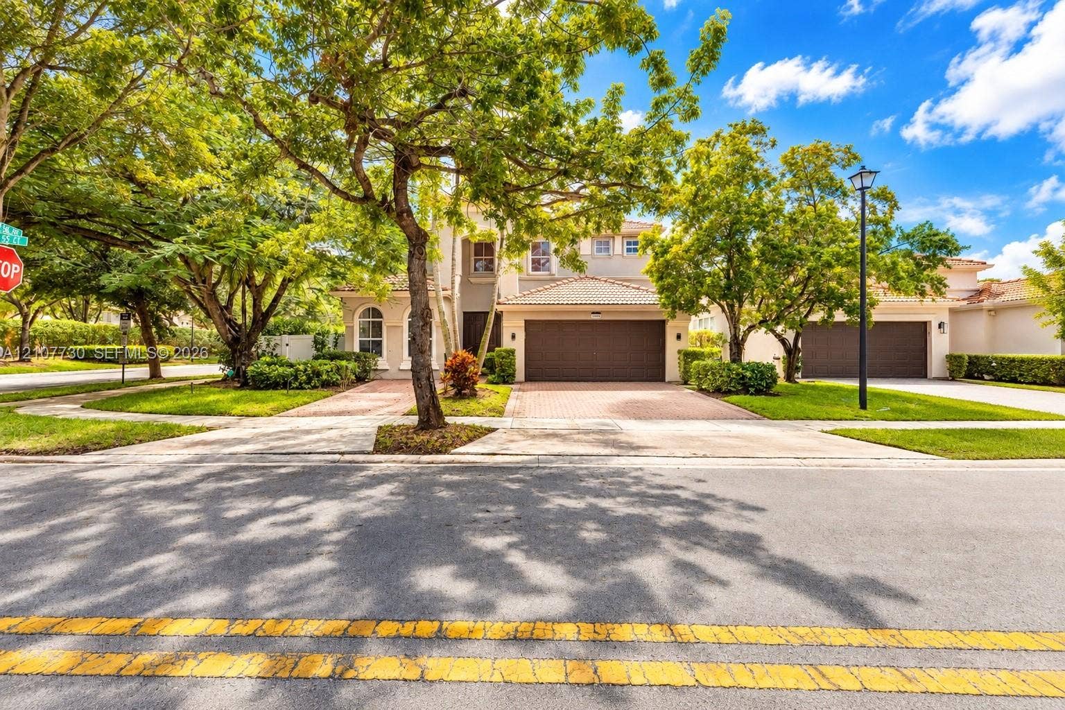 15606 SW 52nd Court, Miramar, FL 33027 Exterior facade featuring a stucco finish, multi-car garage with paneled doors, clay tile roof, and a paved driveway, set amidst mature landscaping