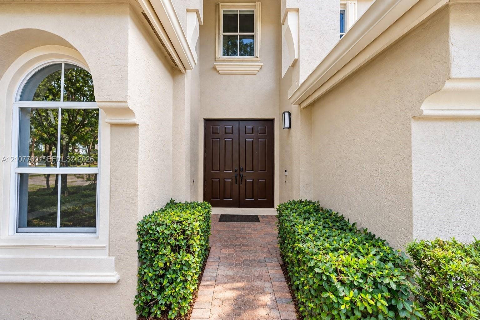 15606 SW 52nd Court, Miramar, FL 33027 Stucco exterior entrance featuring a double-door entry, arched window, stone-paver walkway, and manicured shrubbery
