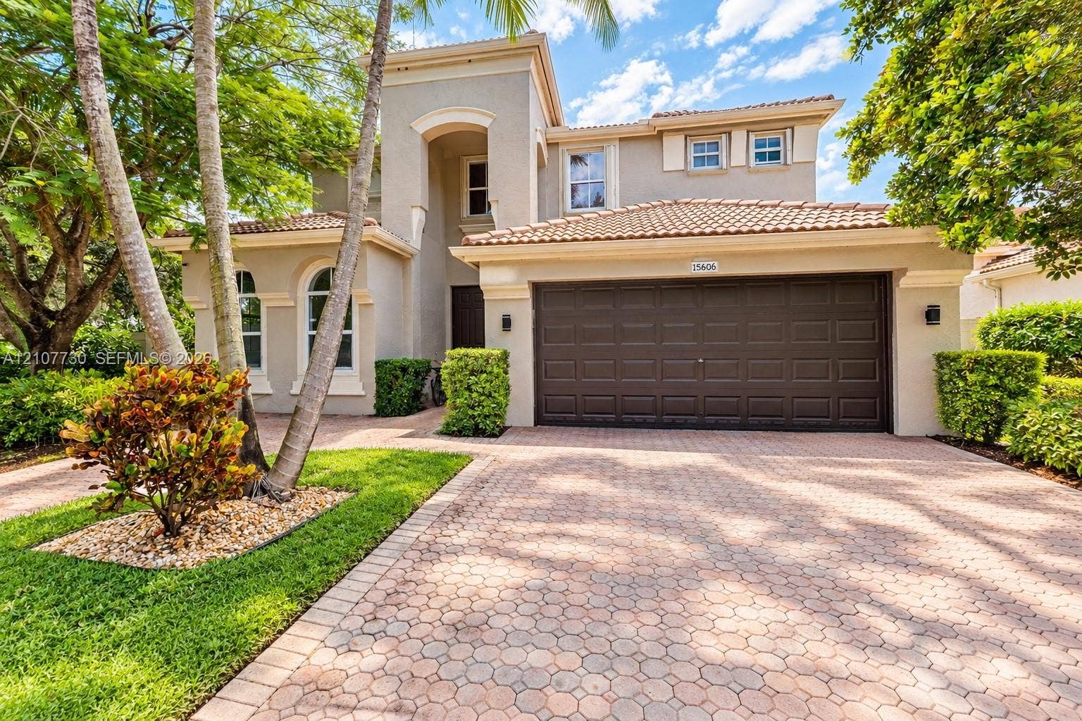 15606 SW 52nd Court, Miramar, FL 33027 Two-story residence featuring a tile roof, stucco exterior, multi-pane arched windows, and a paved stone driveway with an attached two-car garage