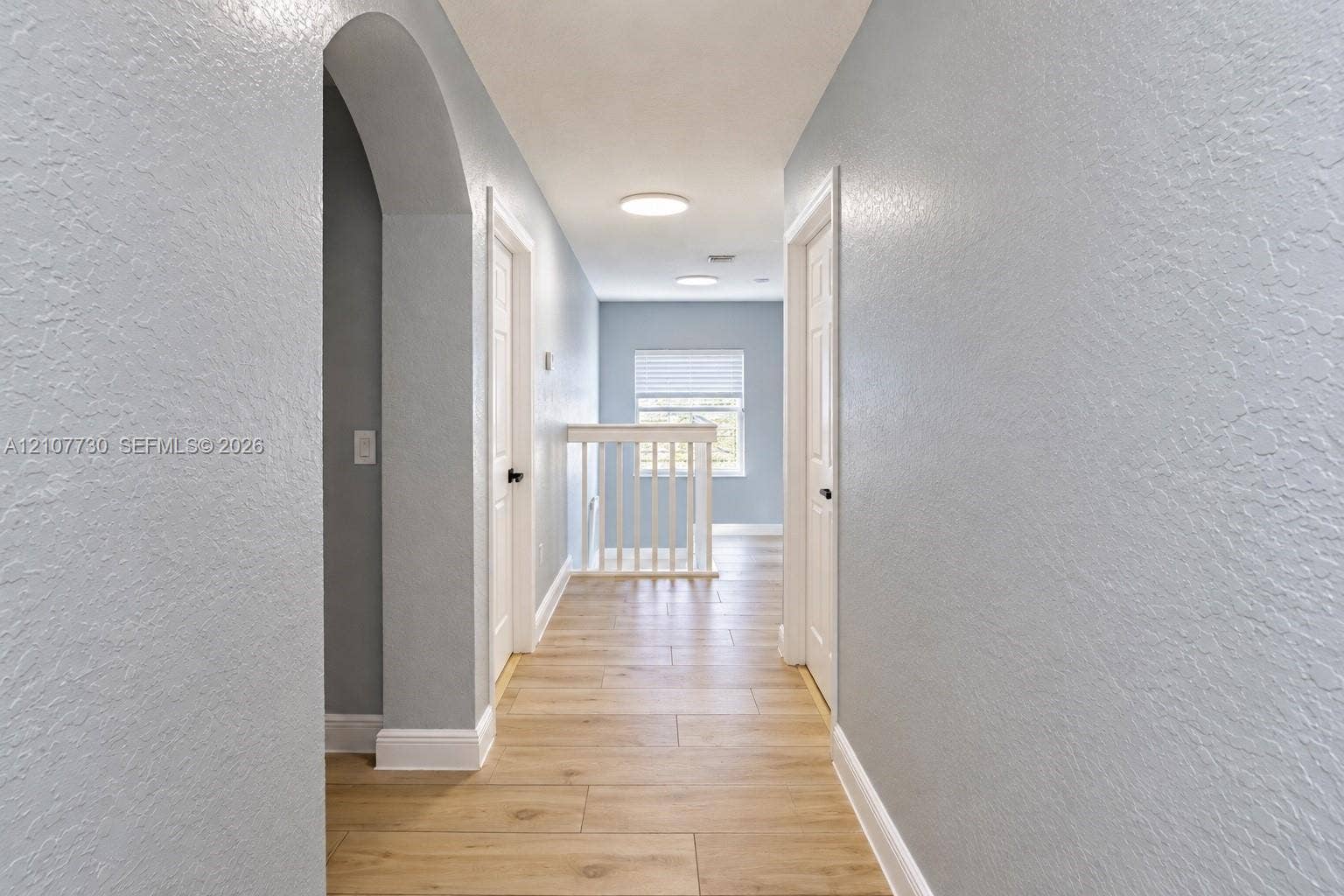 15606 SW 52nd Court, Miramar, FL 33027 Hallway featuring wood-finish flooring, an arched entryway, white paneled doors, recessed ceiling lighting, and a balustrade staircase railing