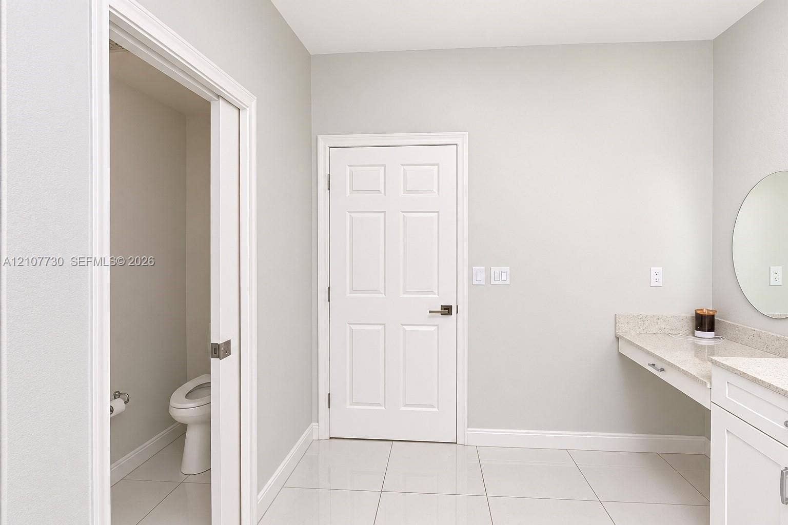 15606 SW 52nd Court, Miramar, FL 33027 Light-toned tile flooring, white six-panel door, built-in vanity with stone-composite countertop, and wall-mounted circular mirror