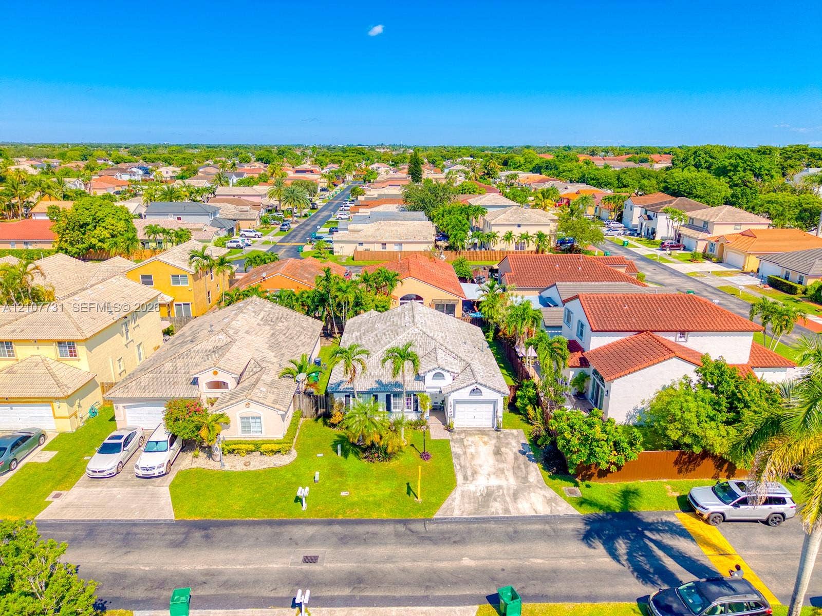 Aerial perspective of a residential property featuring a tiled roof, attached garage, paved driveway, and mature landscaping